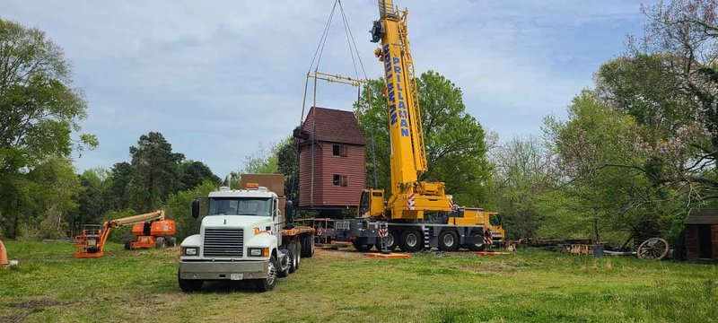 A photo of the historic red windmill being hoisted up and moved by a crane onto a white truck.