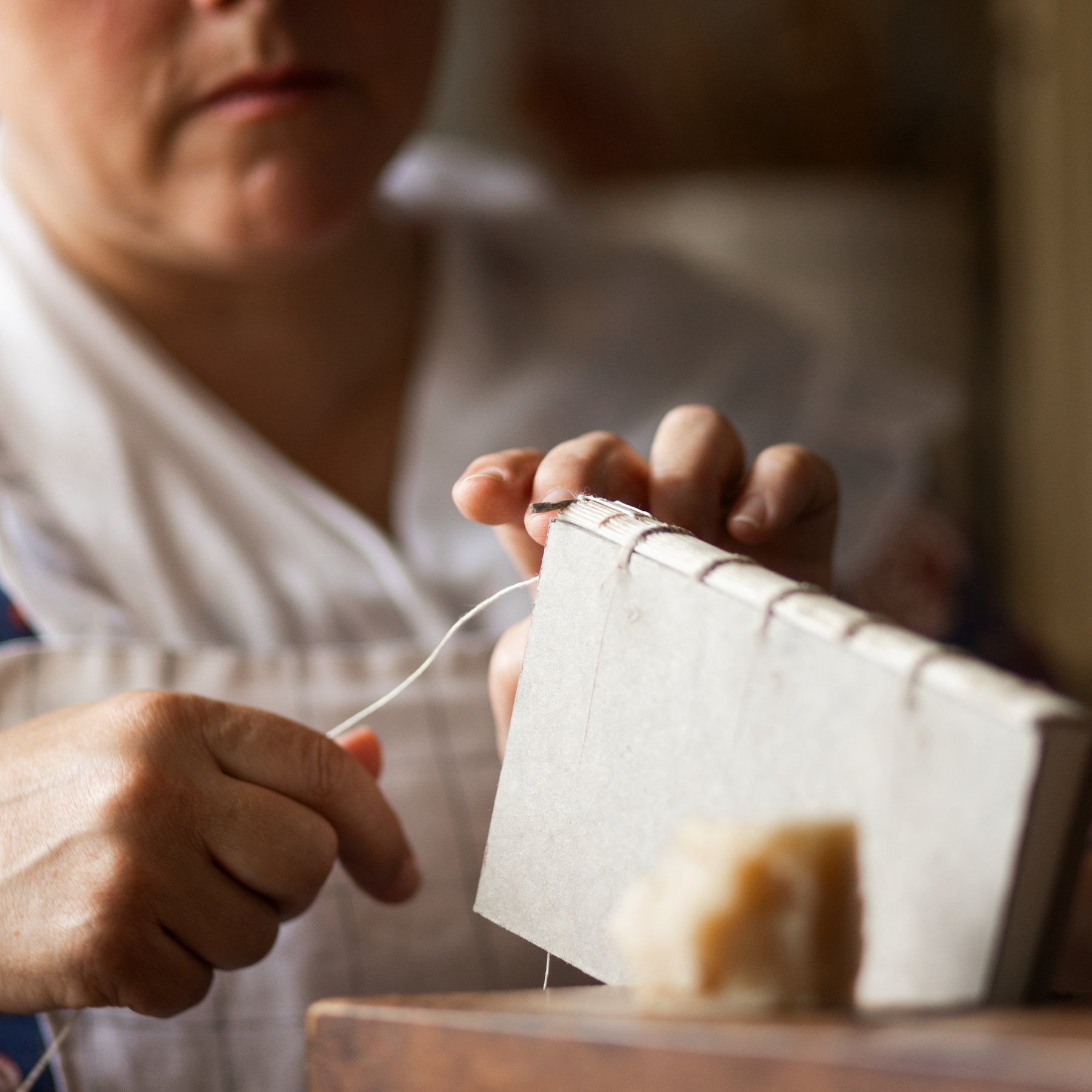 A photo of a bookbinder stitching the binding of a small book.