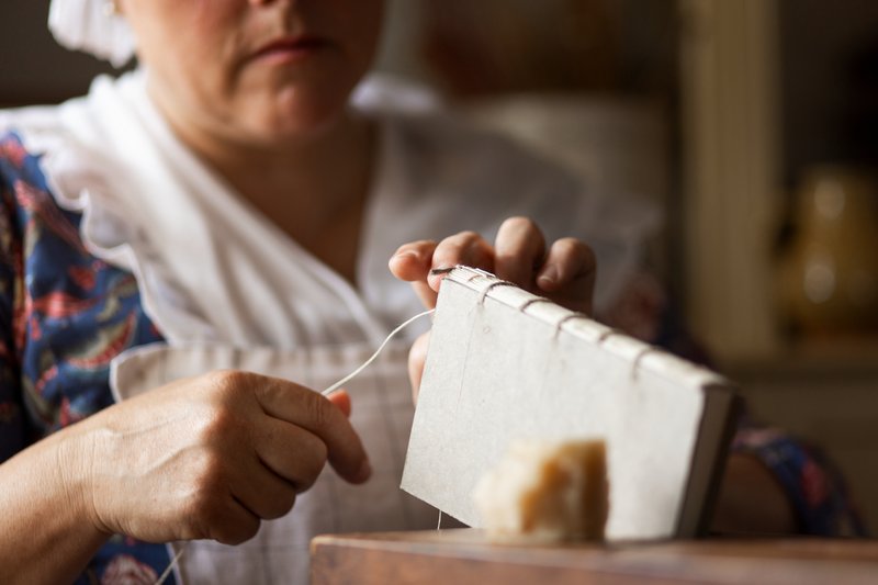 A photo of a bookbinder stitching the binding of a small book.