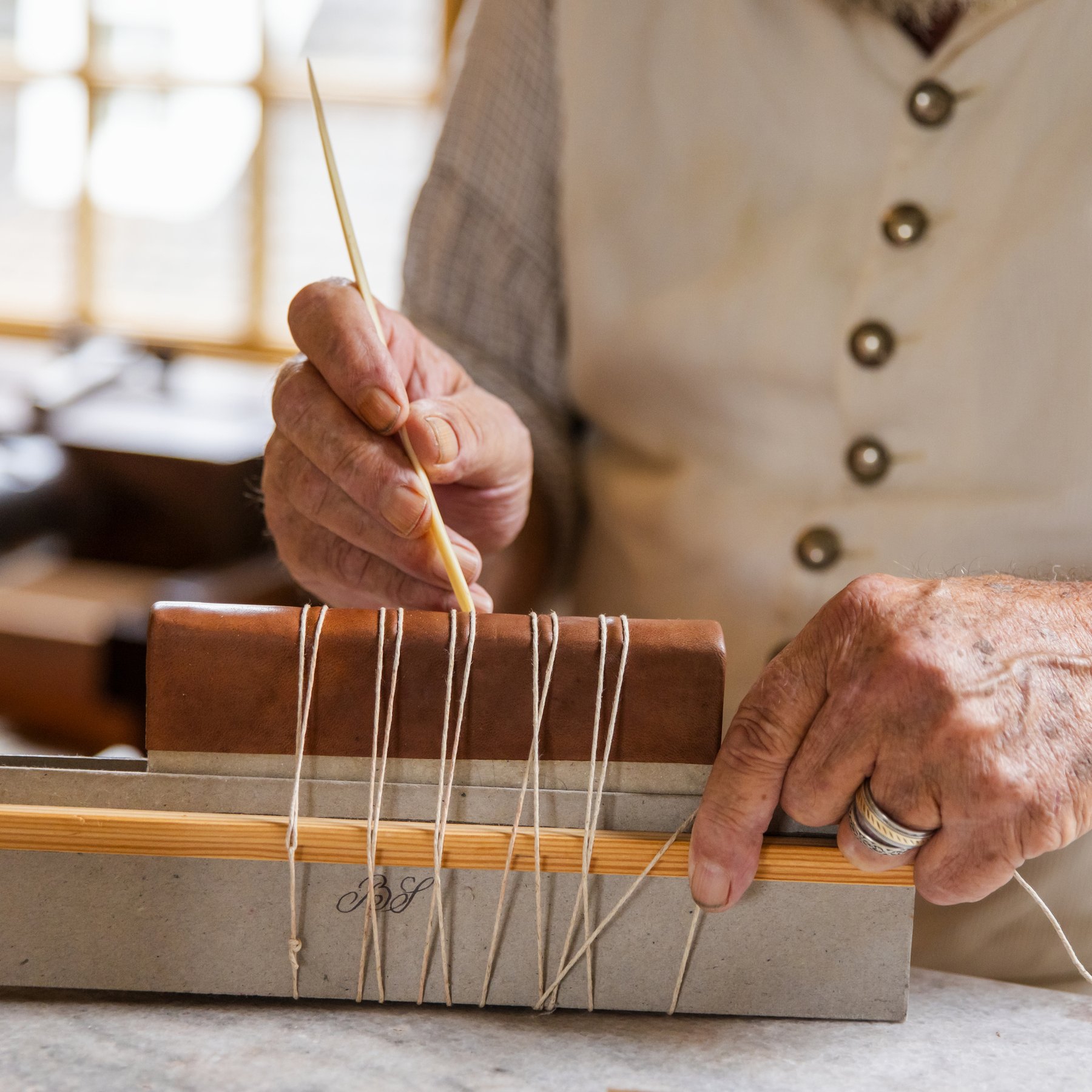 A photo of a bookbinder stitching the binding of a small book.