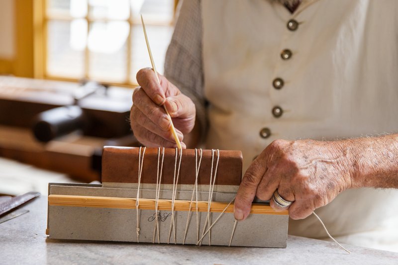 A photo of a bookbinder stitching the binding of a small book.