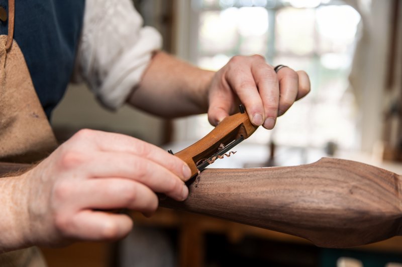 A close up photo of a cabinetmaker shaving the wood on a dressing table.