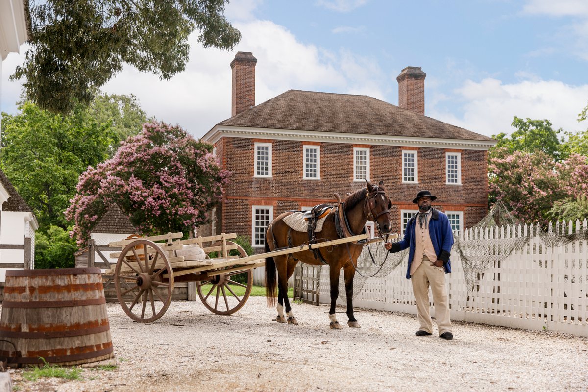 A costumed interpreter stands with a horse and cart outside the George Wythe House in Colonial Williamsburg's Historic Area.