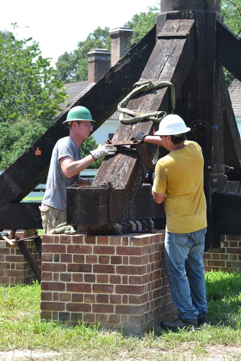 A photo of two construction workers moving an iron brace from the windmill