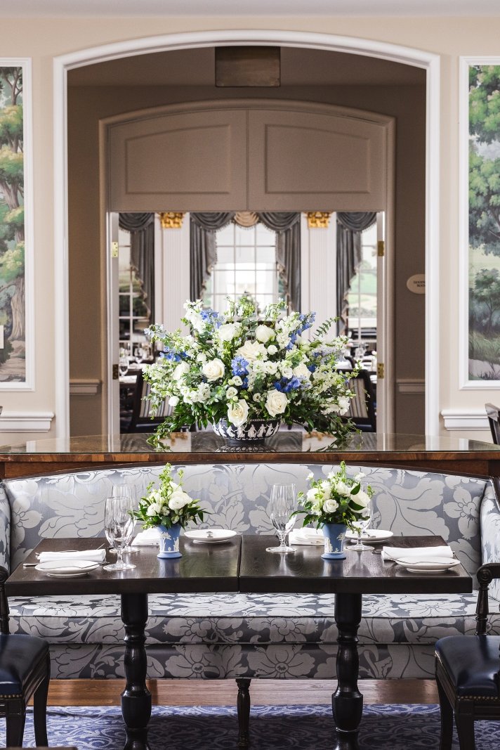 An elegant table is set for breakfast amidst a room decorated with scenic murals and sunlight from the large windows looking out to the gardens of the Williamsburg Inn.