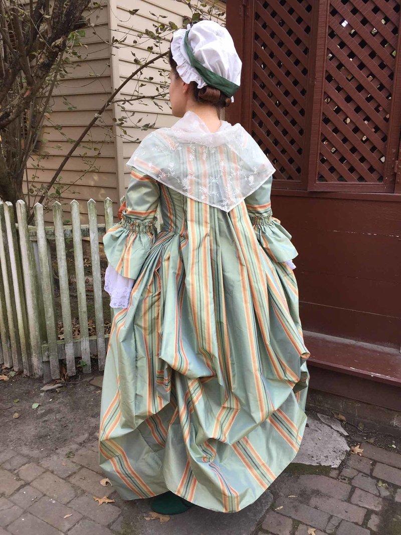 A photo of a woman in an 18th century green and orange dress.