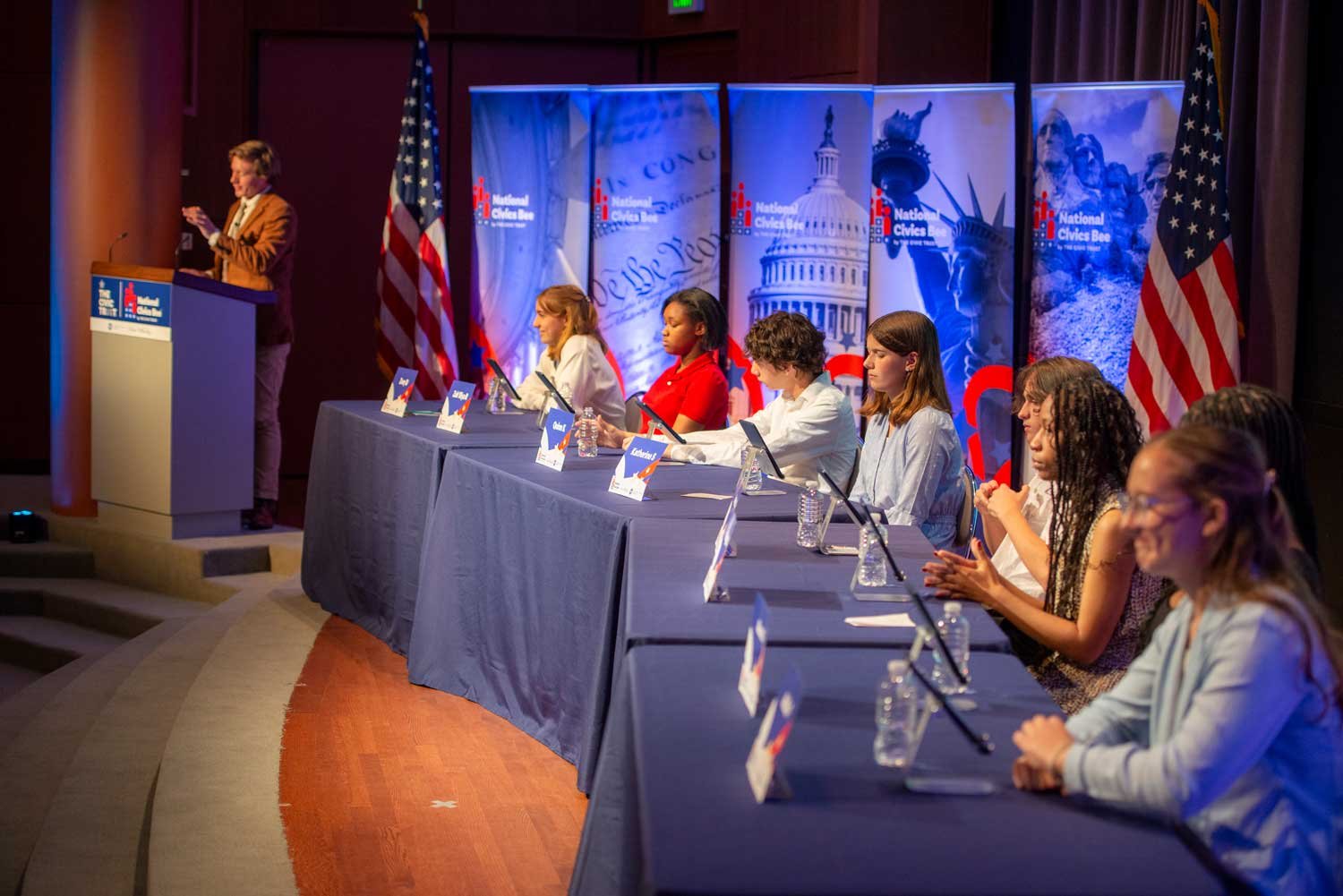 A panel of students sitting at a long table with a presenter on the far left