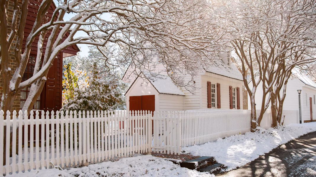 Sun shines through the trees over the snowy roofs of Colonial Williamsburg