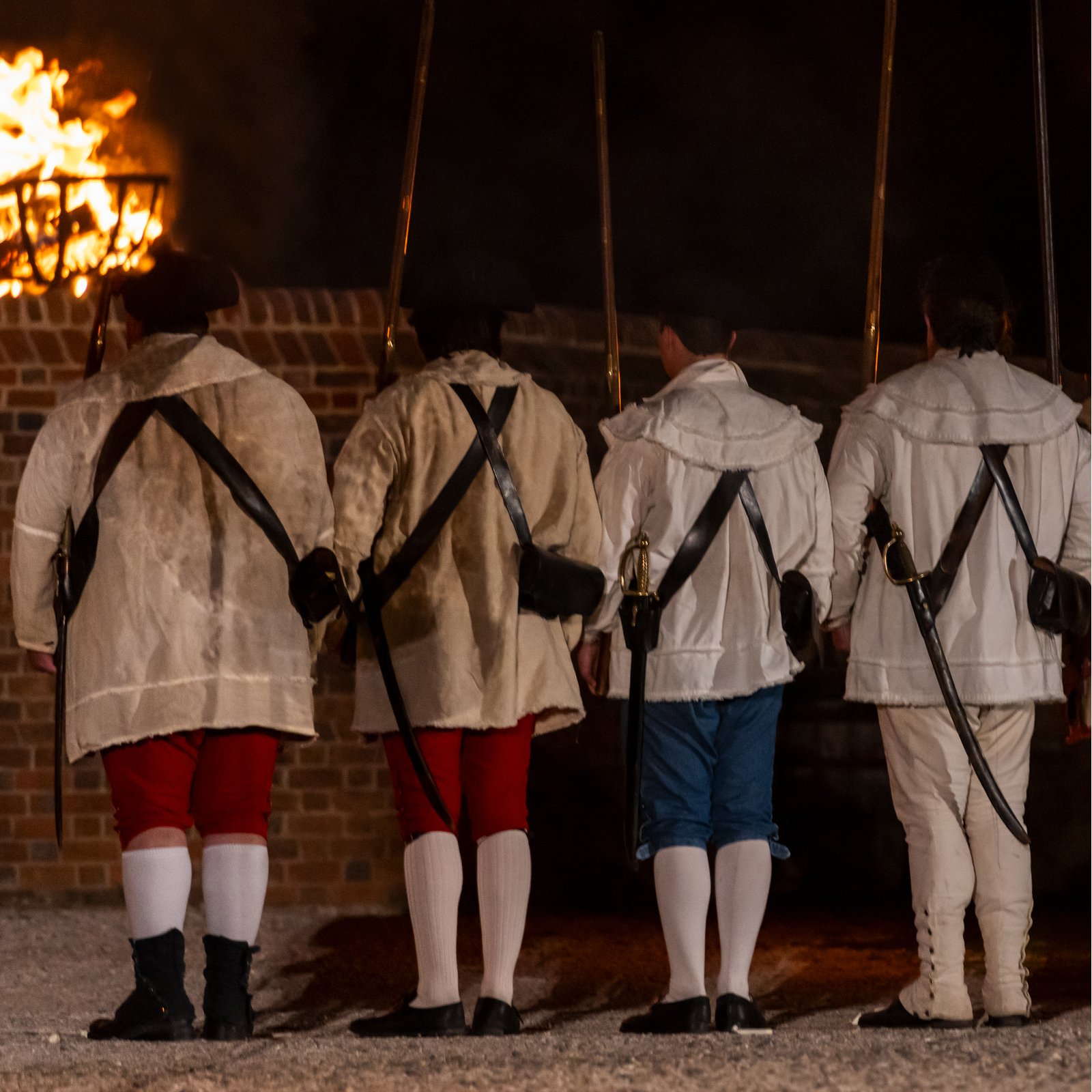 Costumed interpreters stand in front of the Powder Magazine at night.