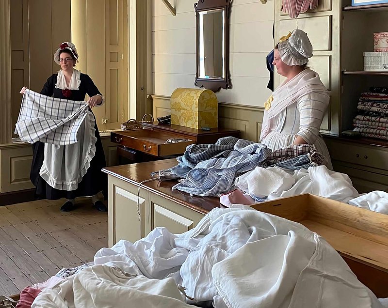 A Photo of two women, dressed in 18th century clothing, in the Colonial Williamsburg Millinery Shop.